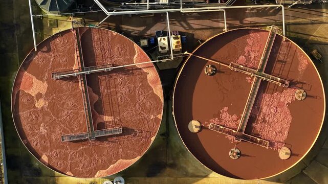 Top down aerial drone view of bubbling activated sludge in industrial vats at a UK wastewater treatment plant for environmental waste management.