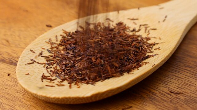 Rooibos tea dried leaves falling down into the wooden spoon close up