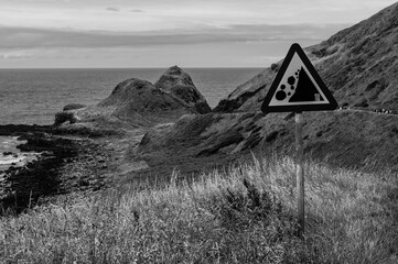 A black and white photo of a beach with a sign warning of a cliff