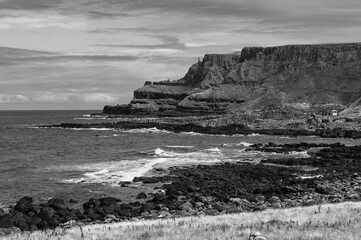 A black and white photo of a rocky shoreline with a calm ocean in the background