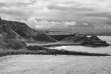 A black and white photo of a rocky shoreline with a cloudy sky in the background
