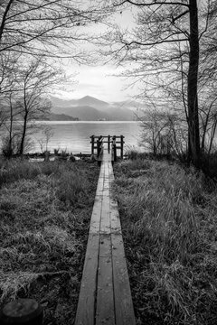 Wooden jetty along the winter water of Orta Lake (piedmont, Northern Italy) with the alps in the background. UNESCO World Heritage Site, its San Giulio island is home to a convent of cloistered nuns.