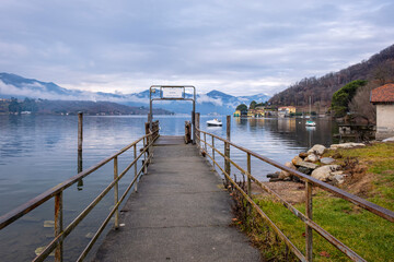 Obraz premium Wooden jetty along the winter water of Orta Lake (piedmont, Northern Italy) with the alps in the background. UNESCO World Heritage Site, its San Giulio island is home to a convent of cloistered nuns.
