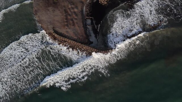 Aerial Drone View of Waves Crashing on a Curved Breakwater in Porto Pino, Sardinia, Italy