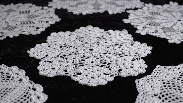 Close-up of white, crocheted doilies arranged on a dark, textured surface, showcasing intricate details