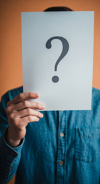 Person holding white paper with question mark, obscuring face, against orange background, symbolizing anonymity, uncertainty, or inquiry