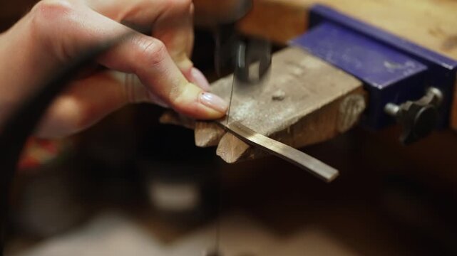 Jeweler cutting silver strip with professional saw.