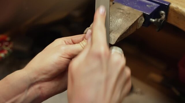 Professional jeweler filing silver ring on workbench.