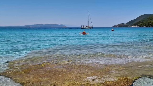 4K Close-up of Crystal Clear Turquoise Water at Milia Beach Skopelos: Sailing Boats and People on Canoe, Sporades Islands Greece, Calm Sea Waves Sound, Summer Travel Greek Islands