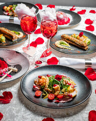 A romantic table setting features exquisite dishes, drinks, and rose petals