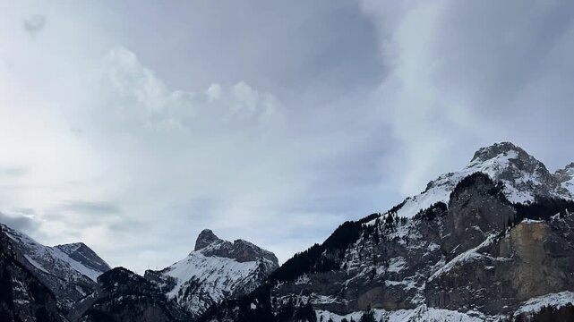 Fast-moving clouds above high and rocky mountains. Time-lapse of the Swiss Alpine landscape on a cold winter day. Snowy mountain peak against a cloudy sky. Kandersteg, Berner Oberland, Switzerland.