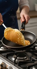 Person flipping a pancake in a black frying pan on a gas stove in kitchen