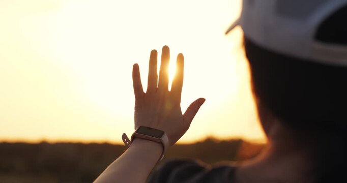 Woman raises hand with smartwatch against sunset light. Female runner checks time on hand wristband. Fitness tracker on hand monitors health outdoors. Active lifestyle girl enjoys sun evening.