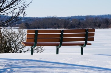 A wooden bench faces frozen lake, inviting reflection in a peaceful winter setting near Greenlane Reservoir, Pennsburg, Pennsylvania, U.S.A
