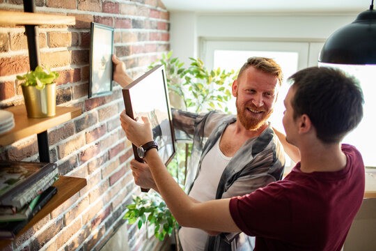 Two men hanging framed pictures at home
