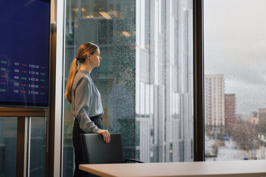 Businesswoman looking out of office window at the rain