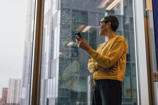 Woman Holding Phone, Gazing at Rainy City View