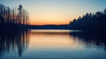 Obraz premium A peaceful lake reflects the colors of dusk with soft ripples on the surface and trees silhouetted along the shoreline under a fading sky
