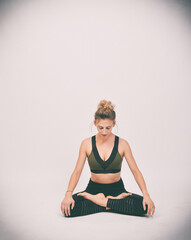 Fototapeta premium Sportliche Frau sitzt in Meditations- und Dehnposition im Studio. Ruhige Yoga- und Pilates-Pose mit Fokus auf Achtsamkeit, Balance und Körperwahrnehmung. Minimalistisches Fitness- und Wellnessmotiv.