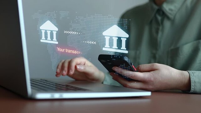 Online banking transaction shown on computer screen with confirmation message and mobile phone in use.