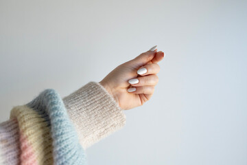 Woman's hand wearing a sweater and white nail polish (stock photo)