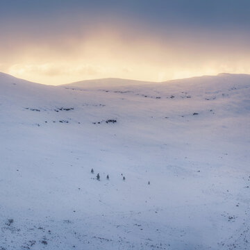 Aerial view of a stark, snow-covered landscape under a sky bruised with twilight hues, a few figures dotting the pristine expanse, Glendalough, County Wicklow, Ireland.
