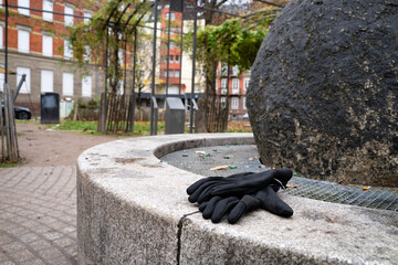 Black gloves resting on the edge of a fountain in a city square. Everyday urban scene showing personal accessories, representing casual style, seasonal life, and city mobility.