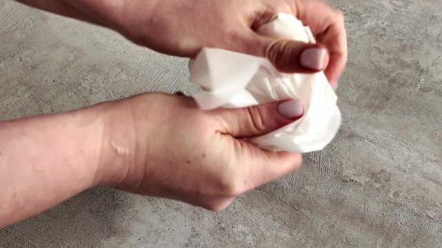 Women's hands crumple a sheet of parchment paper into a tight ball, and then smooth it out again