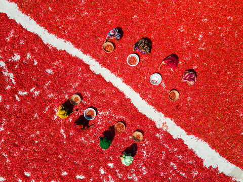Aerial view of vibrant red chilies spread out to dry, contrasting against the white line, with women at work, Bogura, Rajshahi Division, Bangladesh.