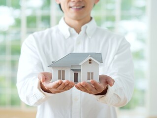 両手で家の模型を大切に持つ男性が伝える住宅購入と安心の暮らしイメージ
