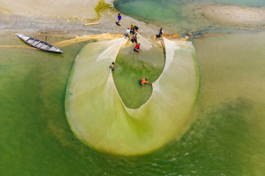 Aerial view of fishermen casting a large net in the river, creating a mesmerizing pattern against the water's surface, Bogura, Rajshahi Division, Bangladesh.