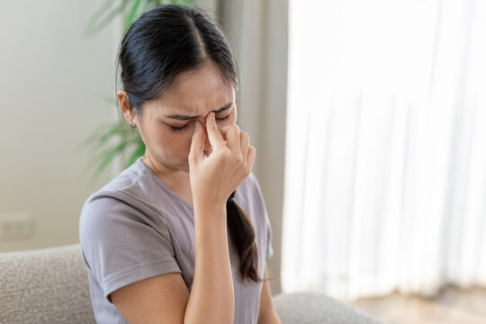 women holding her nose bridge with eyes closed, feeling sinus pain or stress. Concept of sinus pressure, fatigue, headache, tension and discomfort from allergies or overwork at home.