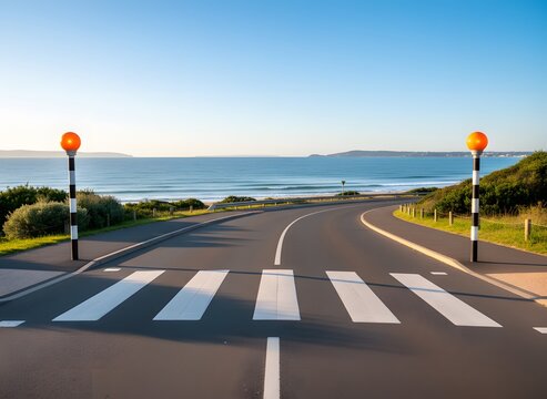 Zebra crossing with orange Belisha beacons on a scenic coastal road overlooking the ocean and beach at golden hour