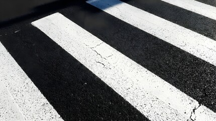 High contrast diagonal white pedestrian stripes on weathered dark asphalt road surface