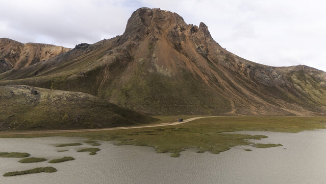 Aerial view of the stark, rugged mountain looms over the flat marshland where the water reflects the cloudy sky, Selfoss, Iceland.