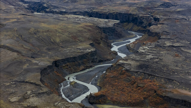 Aerial view of a stark river cutting through the rugged landscape, a symphony of greys and browns under the cold Icelandic sky, Selfoss, Iceland.