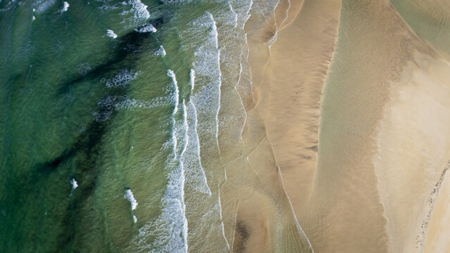 Aerial view of the meeting of the dark green ocean and the light beige sand, creating a beautiful contrast of colors and textures, Selfoss, Iceland.