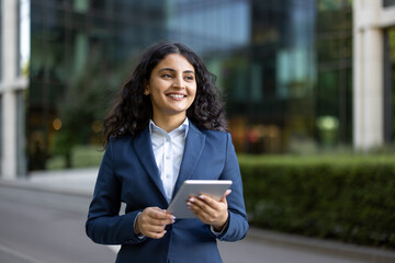 Professional businesswoman smiling confidently holding digital tablet walking outdoors