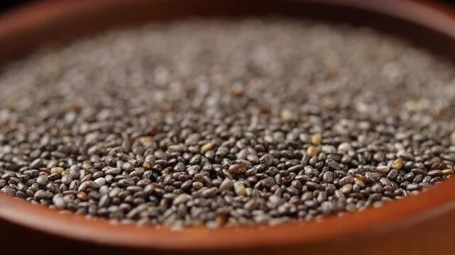 Close-up of raw chia seeds in a brown wooden bowl rotating on a black background.