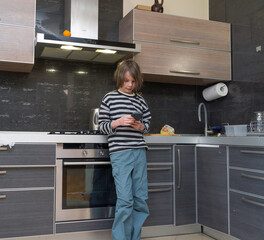 Young boy using a smartphone in a modern kitchen. Child looking at mobile phone screen