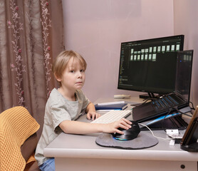 Young boy sitting at desk using computer mouse. Child learning online at home with laptop