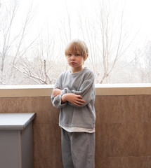 Serious young boy with arms crossed on a balcony. Portrait of an unhappy child in winter