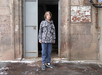 Young boy standing at old building entrance. Urban child portrait in grey jacket