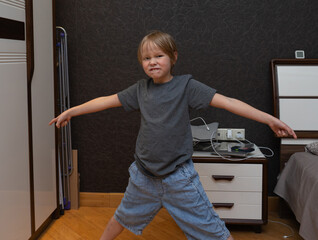 Playful young boy making a funny grimacing face in a bedroom. Child with arms outstretched