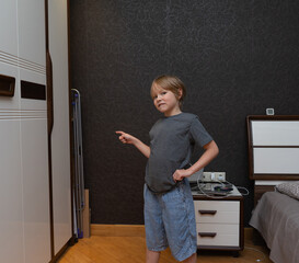 Young boy pointing finger to the side in a bedroom. Child gesturing towards copy space