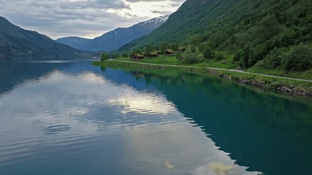 Calm Lovatnet Lake reflecting clouds and mountains in Loen Valley, Norway. Still water and soft light convey quiet Scandinavian summer serenity.