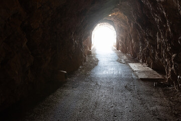 Fototapeta premium A dark rock tunnel opens to bright daylight