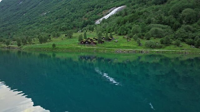 Aerial glide above Lovatnet Lake near Loen, Norway. Clear water, green hills and gentle ripples evoke calm Nordic nature.