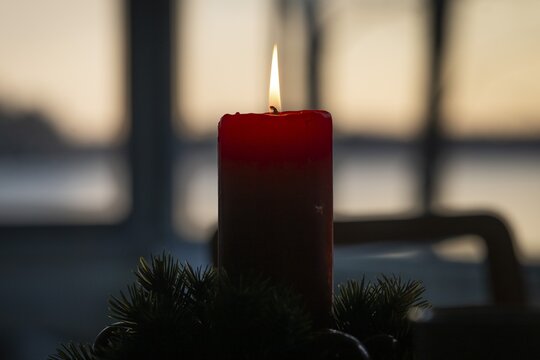 A single red candle in an advent wreath burns in front of a window at dusk and creates a cozy atmosphere, Finland