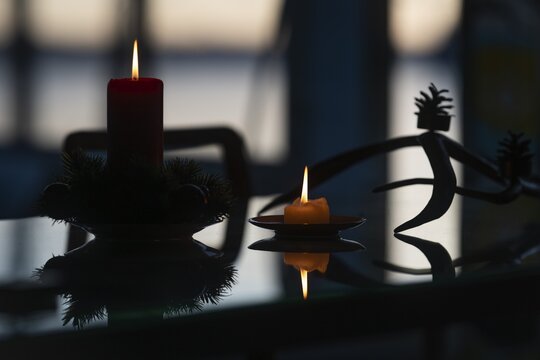 Two candles stand on a table in front of a window at dusk and create a Christmas atmosphere, plus pine branches and pine cones, Finland